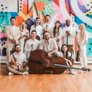 2 rows of musicians holding string instruments in front of a colorful graphic background