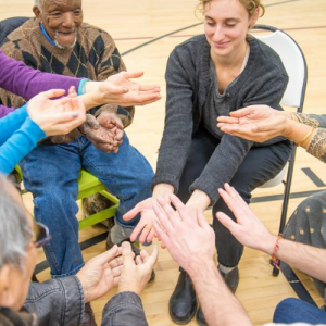 people sitting in a circle with hands raised into the center