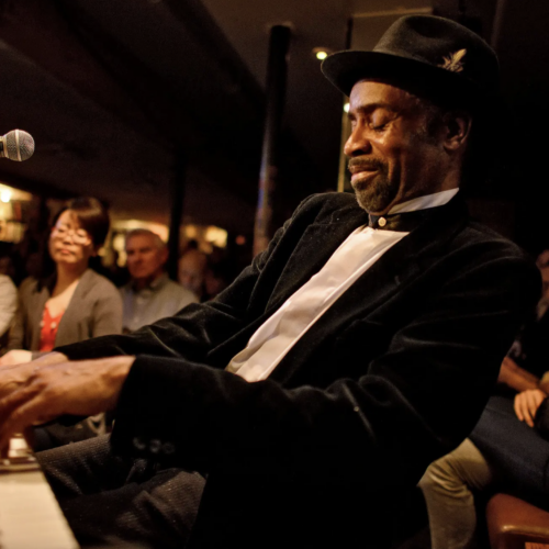 Johnny O'Neal wearing a suit and top hat playing the piano