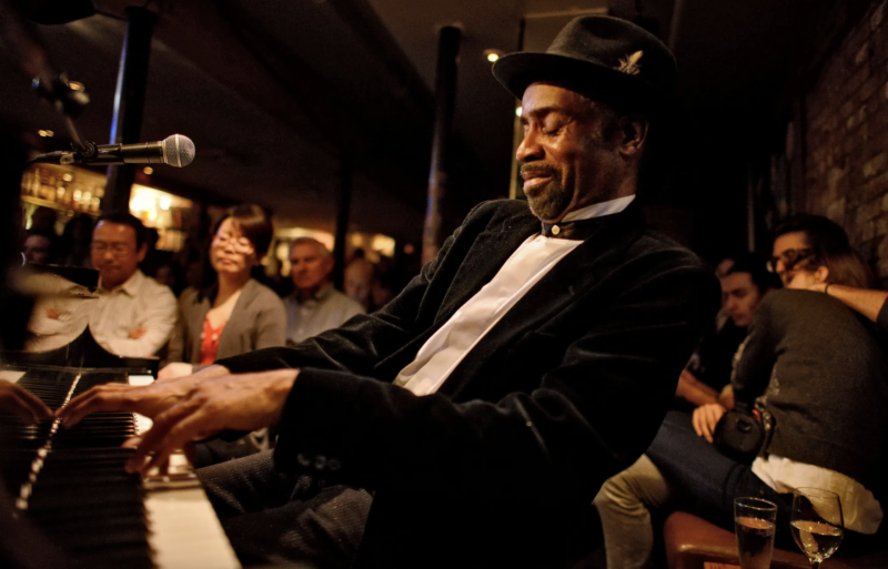 Johnny O'Neal wearing a suit and top hat playing the piano